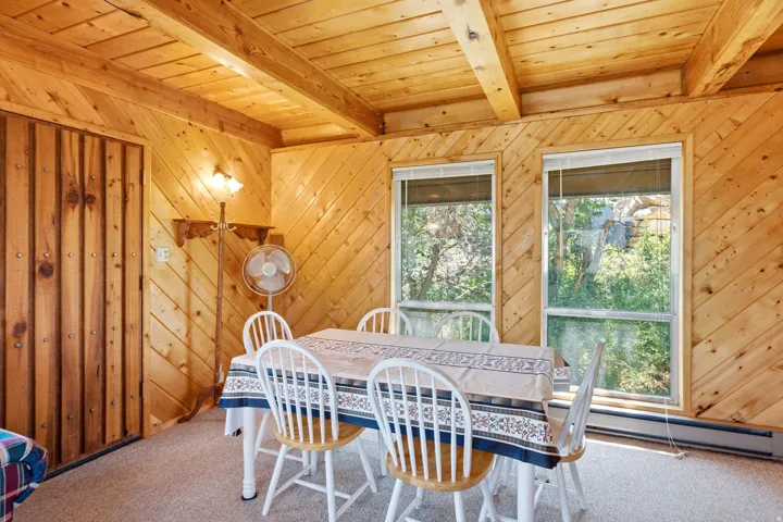 Wood-paneled room featuring a beamed ceiling, two large windows with blinds, and light-colored carpet