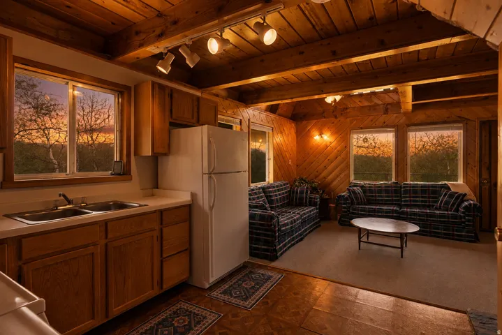Open-concept living area featuring a kitchen with wood cabinetry and a double basin sink, exposed wood beam ceiling, and wood-paneled walls