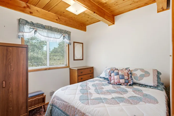 Windowed room featuring a natural wood plank ceiling with exposed beams, white walls, and a window with blinds