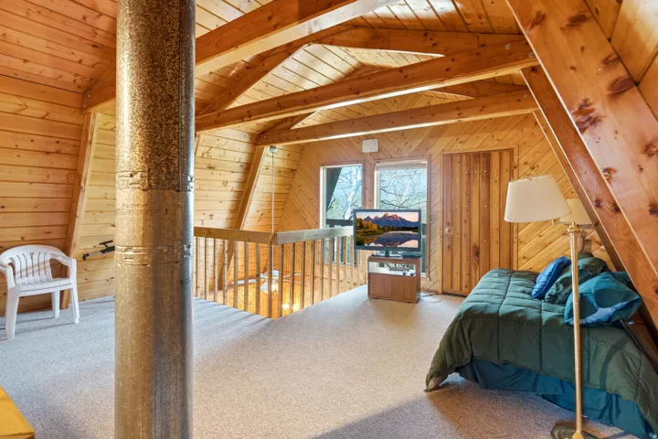 Loft space featuring extensive natural wood paneling, exposed wood beams, a galvanized metal column, and two fixed windows