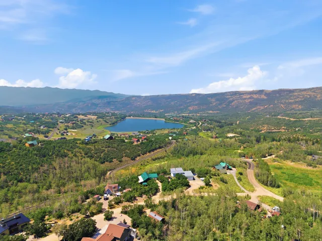 Expansive aerial showcasing a serene lake surrounded by a verdant landscape and distant mountains