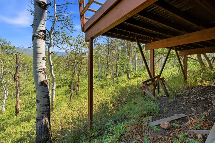 Elevated deck structure featuring natural wood supports, overlooking a verdant hillside with mature aspen trees and dense foliage