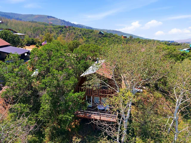 Hillside property featuring a wood-sided exterior, a multi-level deck, and a brown metal roof, surrounded by mature trees