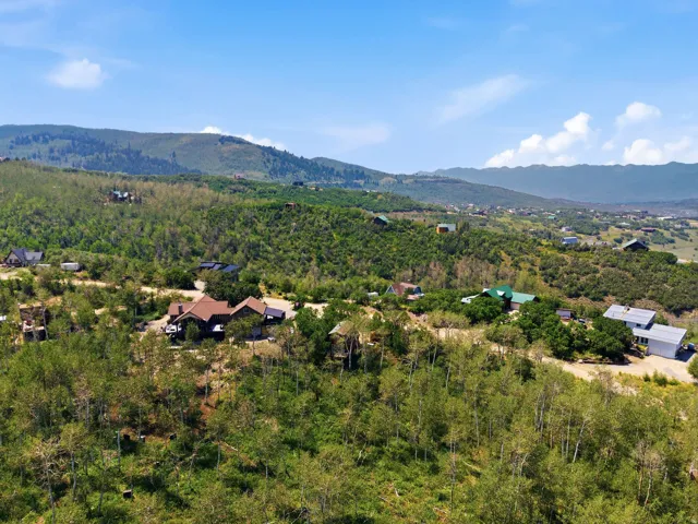 Expansive mountain property featuring a large residence with a dark roof, surrounded by mature trees and lush green hills