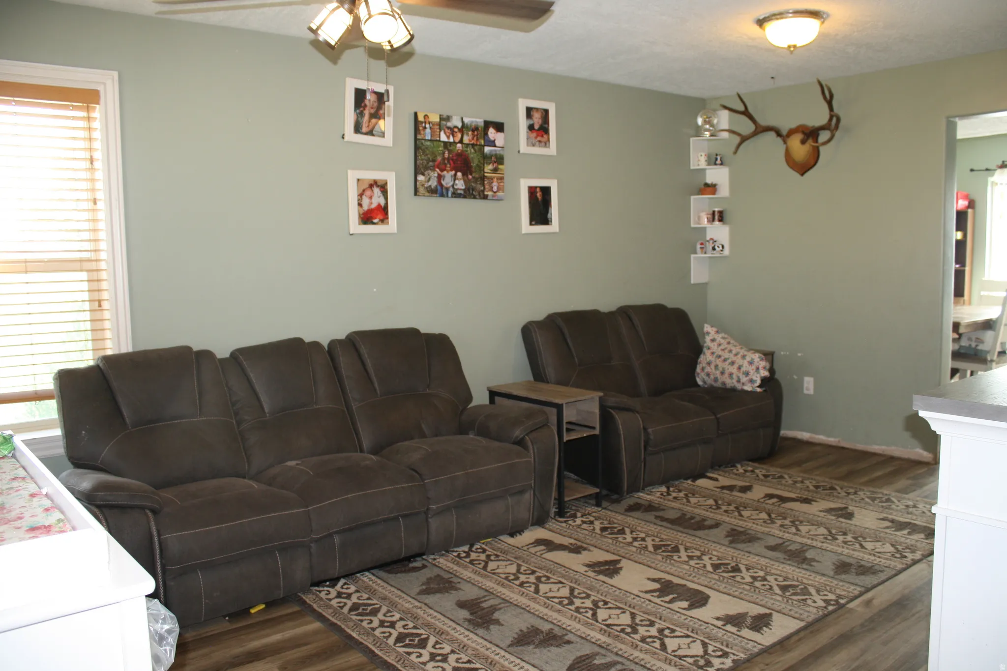 Living space with wood-finish flooring, a ceiling fan with integrated lighting, and a window featuring horizontal blinds