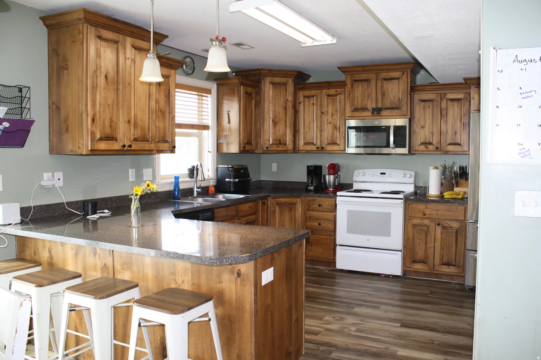 Spacious kitchen featuring extensive wood cabinetry, dark countertops, a built-in microwave, white electric range, and wood-finish flooring