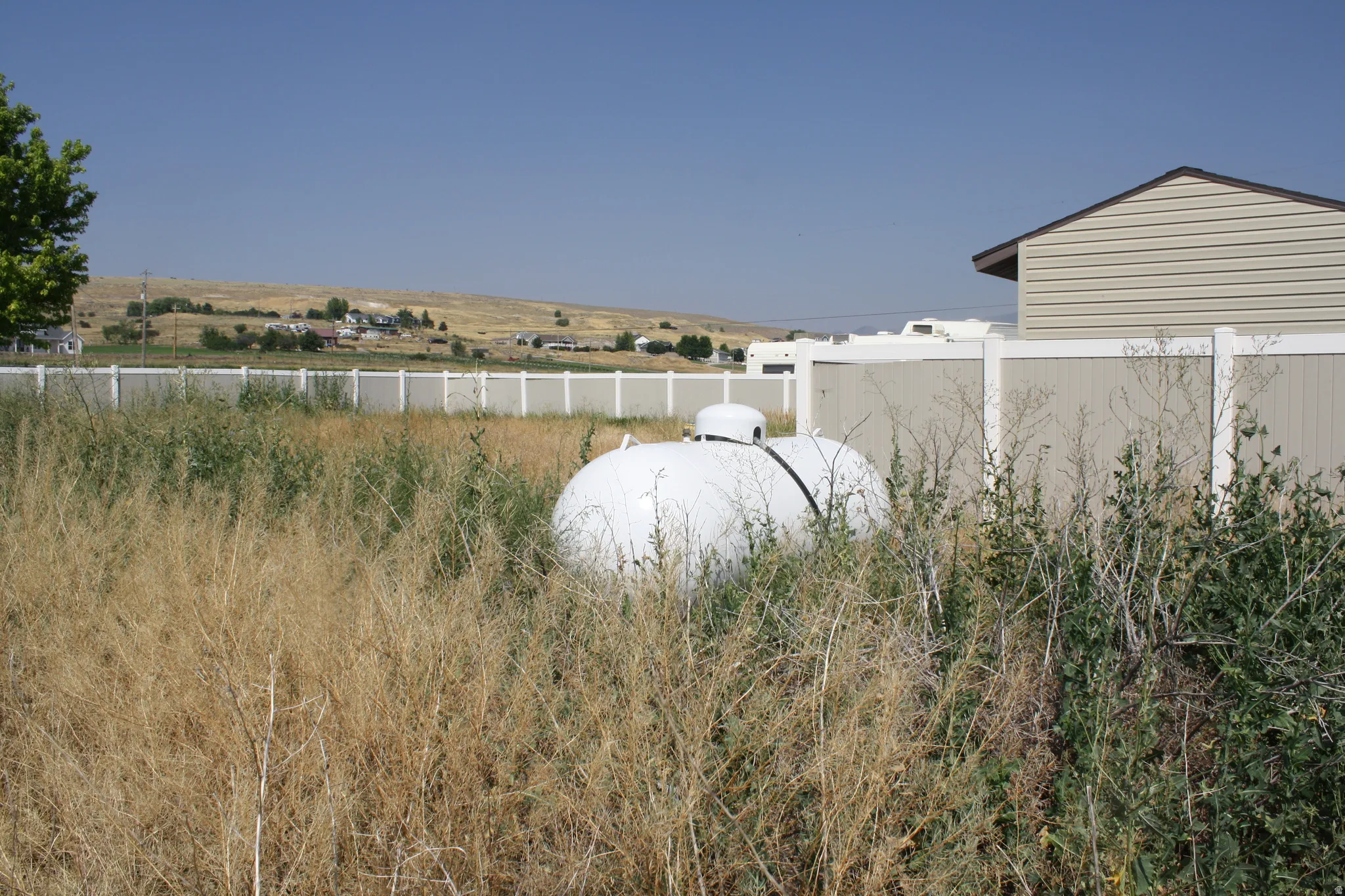 Property boundary defined by a combination of vinyl and wood fencing, with a large white propane tank situated within the lot