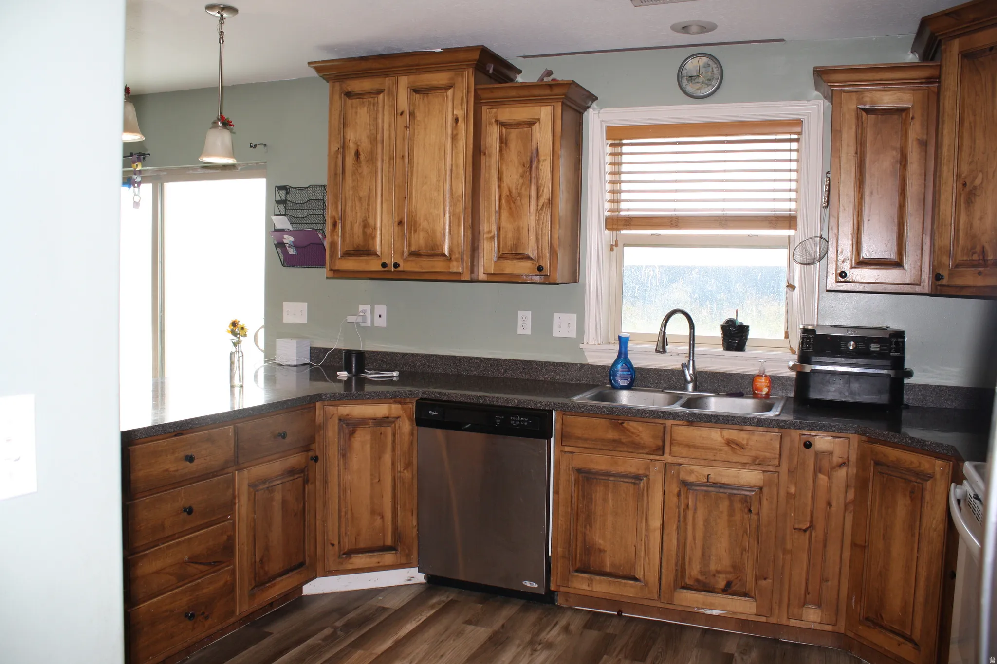 Kitchen featuring wood-finish cabinetry, dark countertops, a double basin sink with a gooseneck faucet, a stainless steel dishwasher, and wood-finish flooring