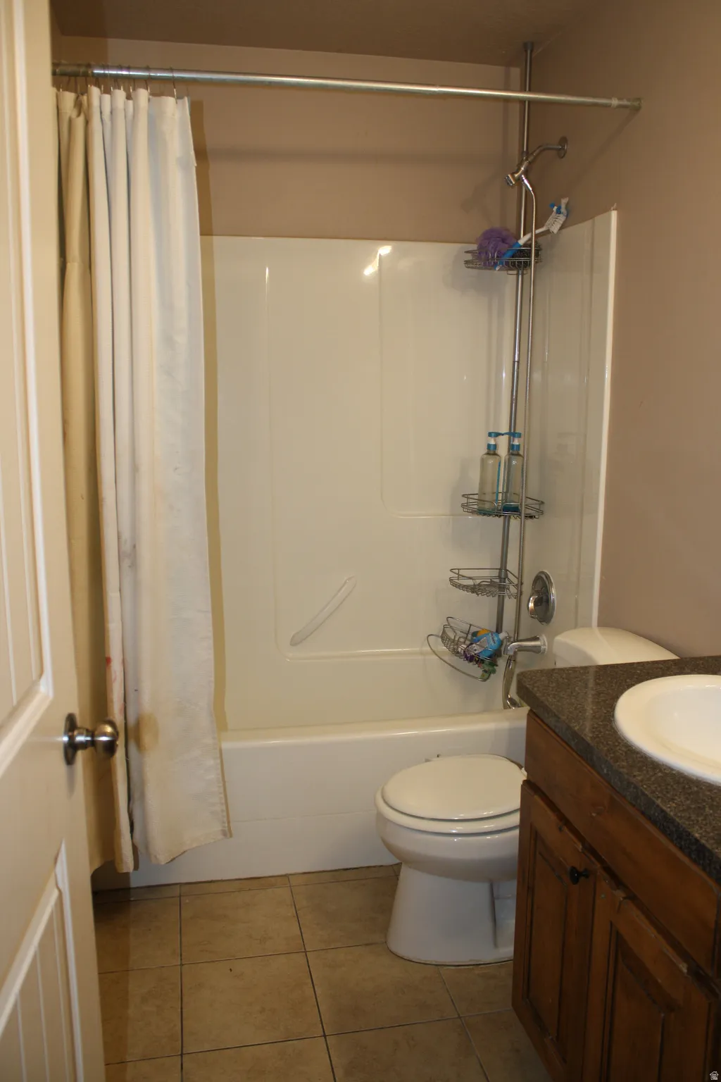Bathroom featuring a white tub/shower combination, toilet, and vanity with a dark countertop and integrated sink