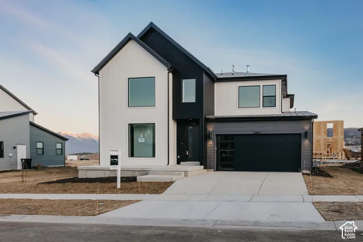 Modern multi-level exterior featuring vertical board-and-batten siding, horizontal lap siding, a concrete driveway, and an attached multi-car garage with glass paneling