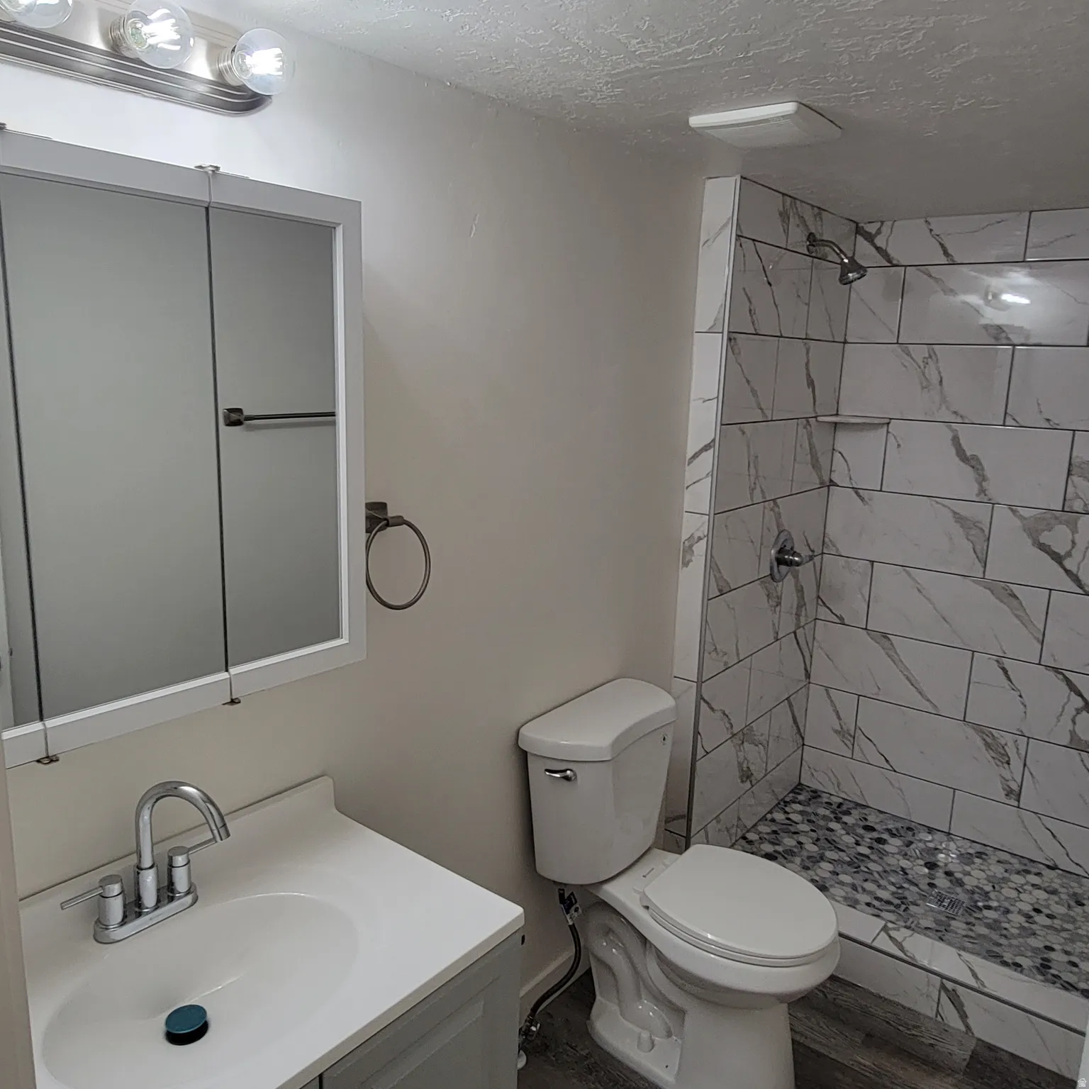 Bathroom featuring a walk-in shower with large format marbled tile, mosaic pebble shower floor, and a built-in shower niche