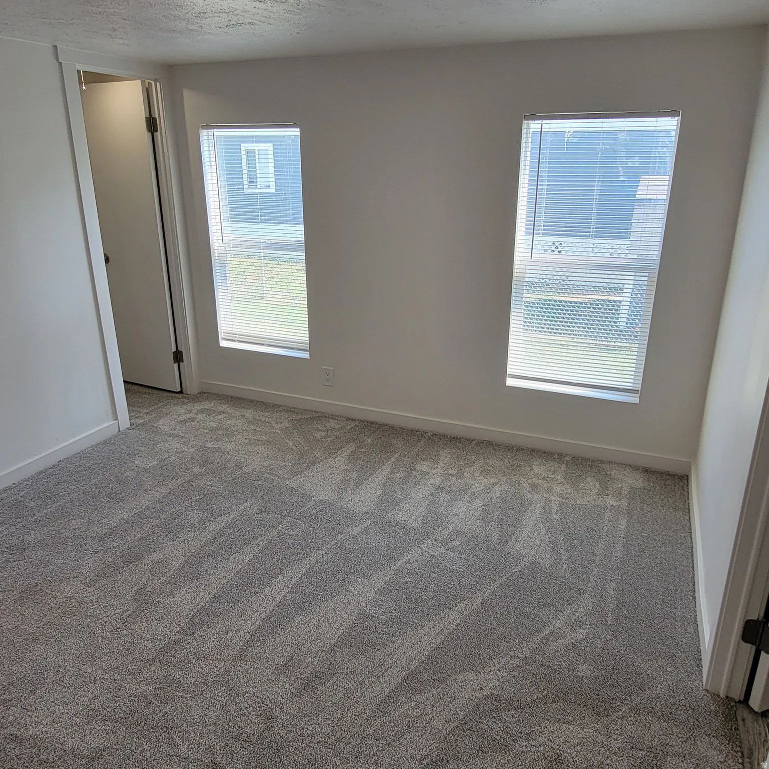 Carpeted room featuring two windows with horizontal blinds, white walls, and white baseboards