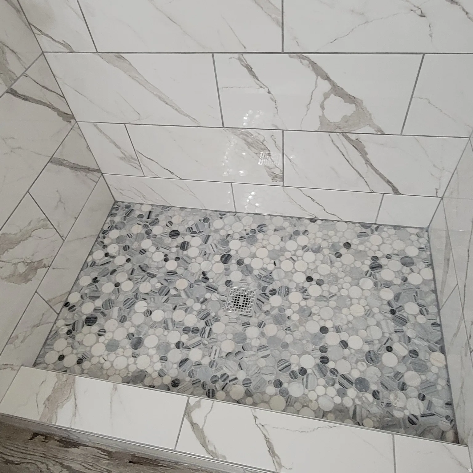 Shower stall featuring large format white tiled walls with grey veining
