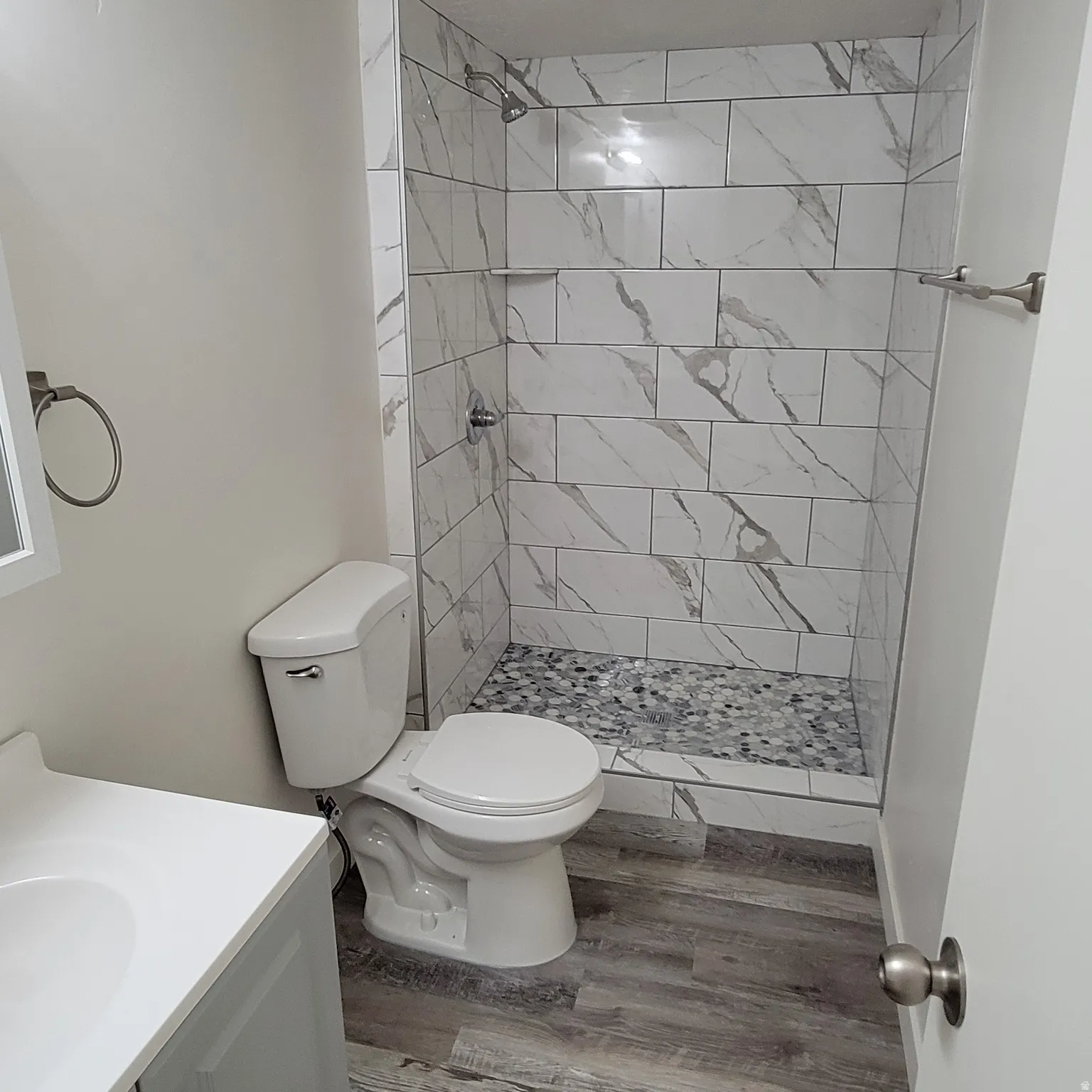 Shower stall featuring rectangular white and gray veined tile walls and a pebble-style floor
