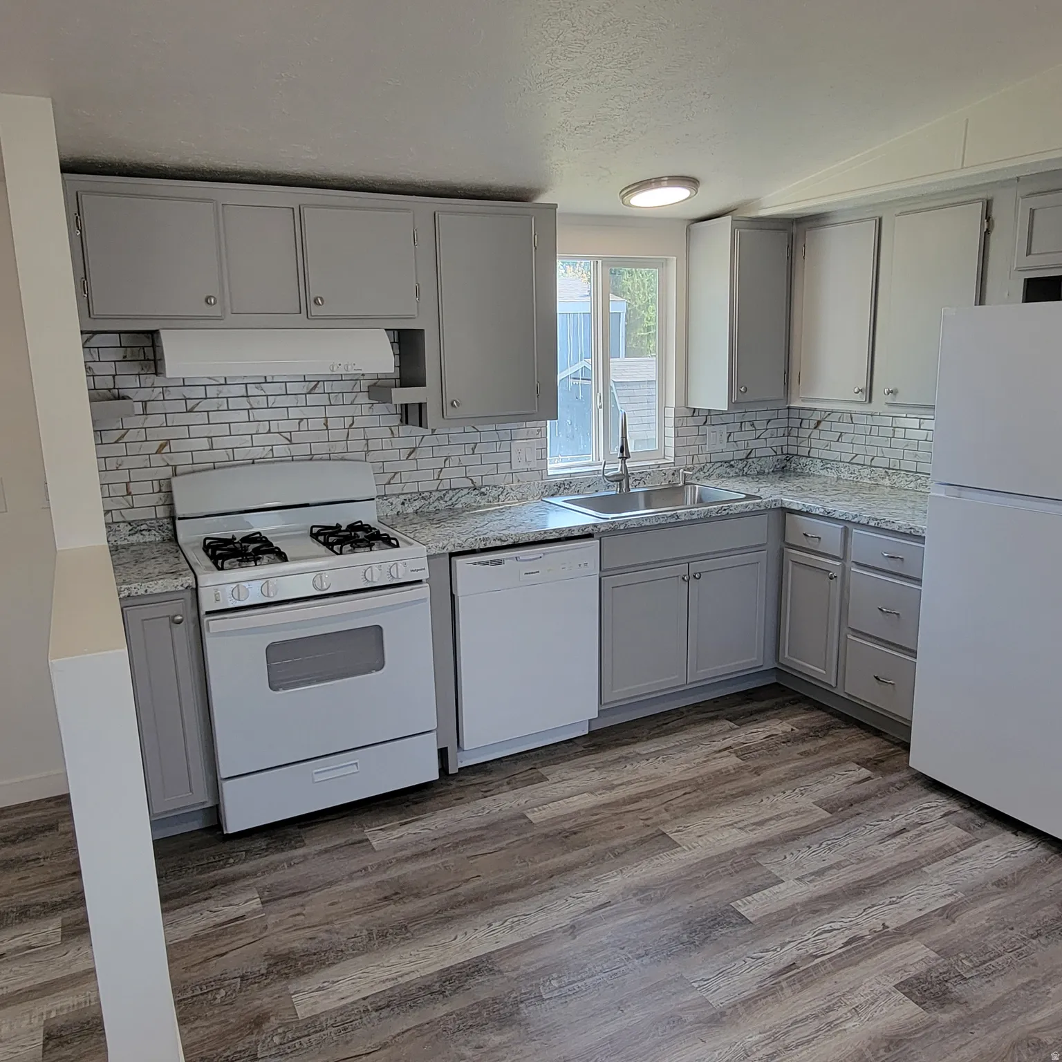 Kitchen featuring wood-finish flooring, white appliances, grey cabinetry, a white subway tile backsplash, and light-toned countertops