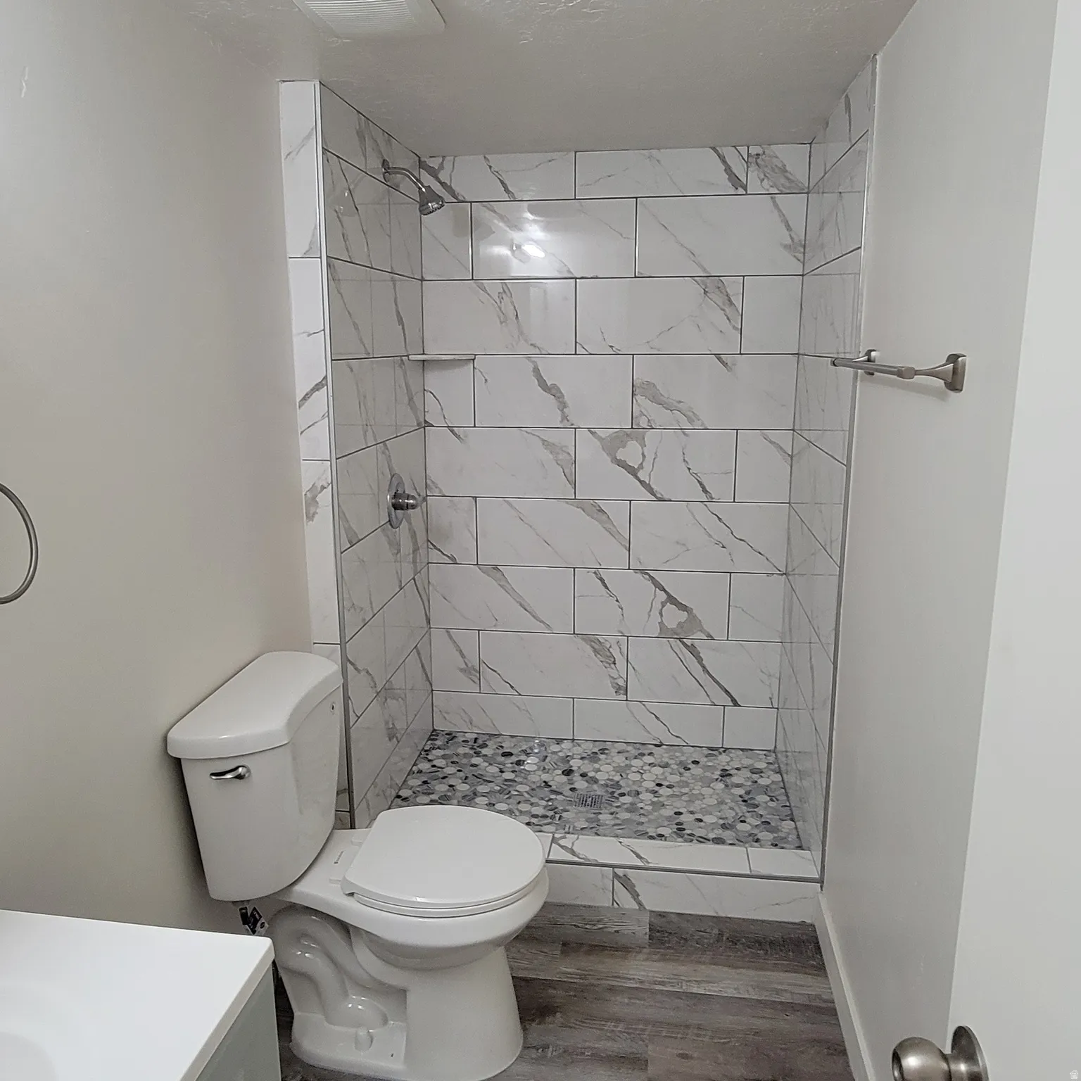 Walk-in shower with marble-look tile surround and mosaic pebble flooring