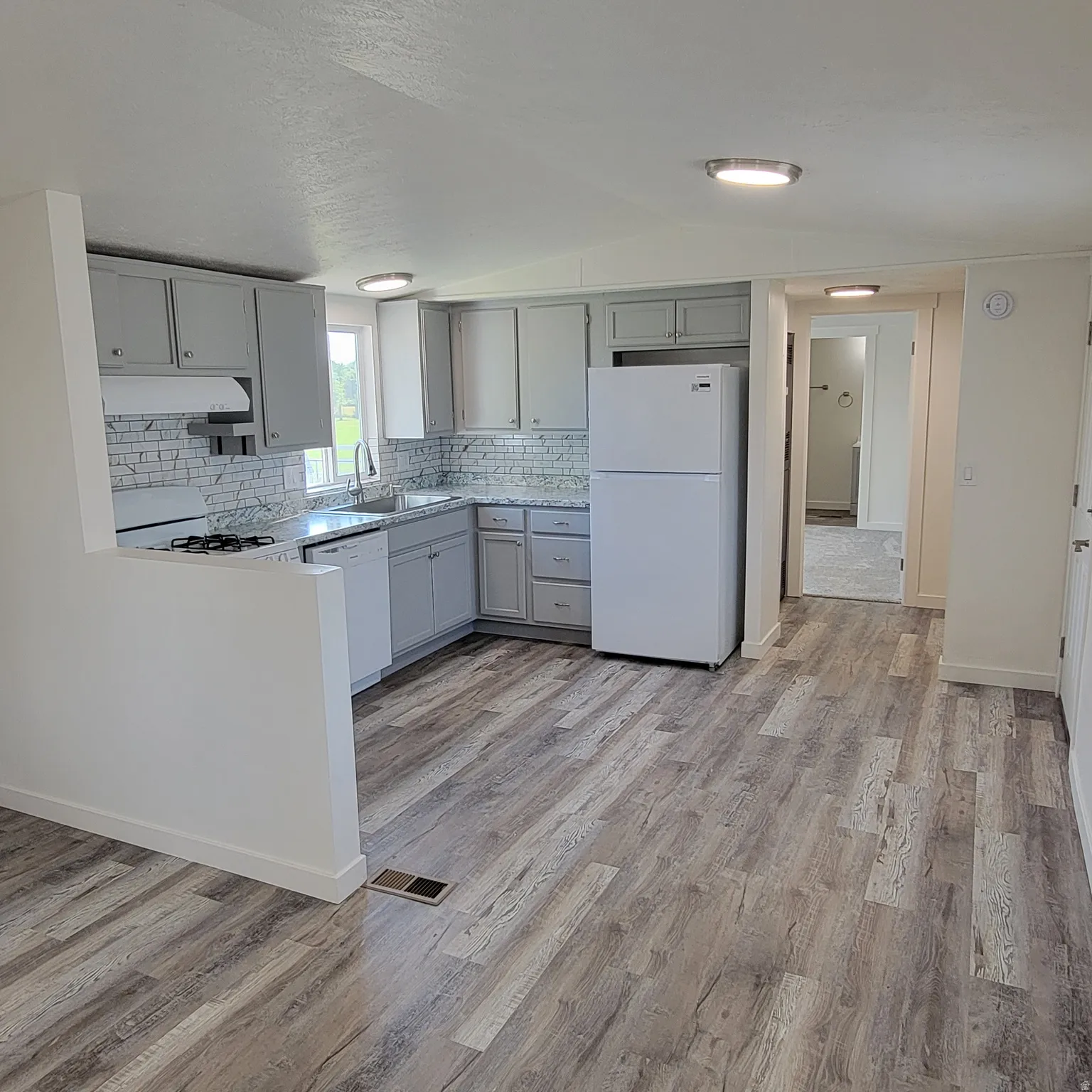 Kitchen with wood-finish flooring, light grey cabinetry, white subway tile backsplash, white appliances, and recessed lighting