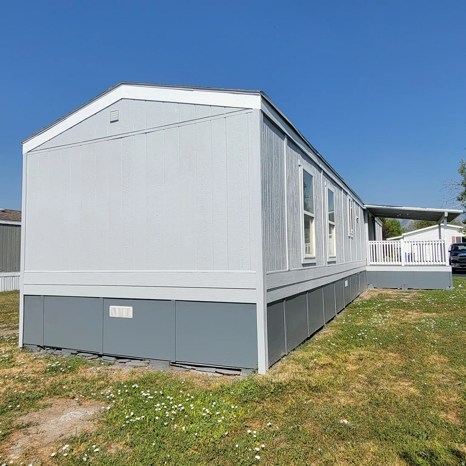 Light gray horizontal siding with white trim, gray skirting, multiple windows, and an attached white-railed porch with a gray floor