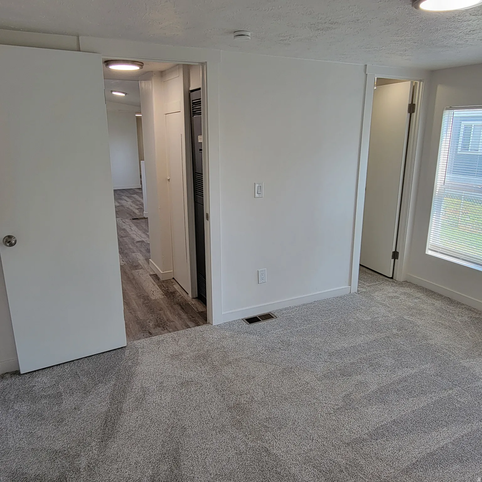 Carpeted room featuring a white interior door with brushed nickel hardware, a window with blinds, and white baseboards