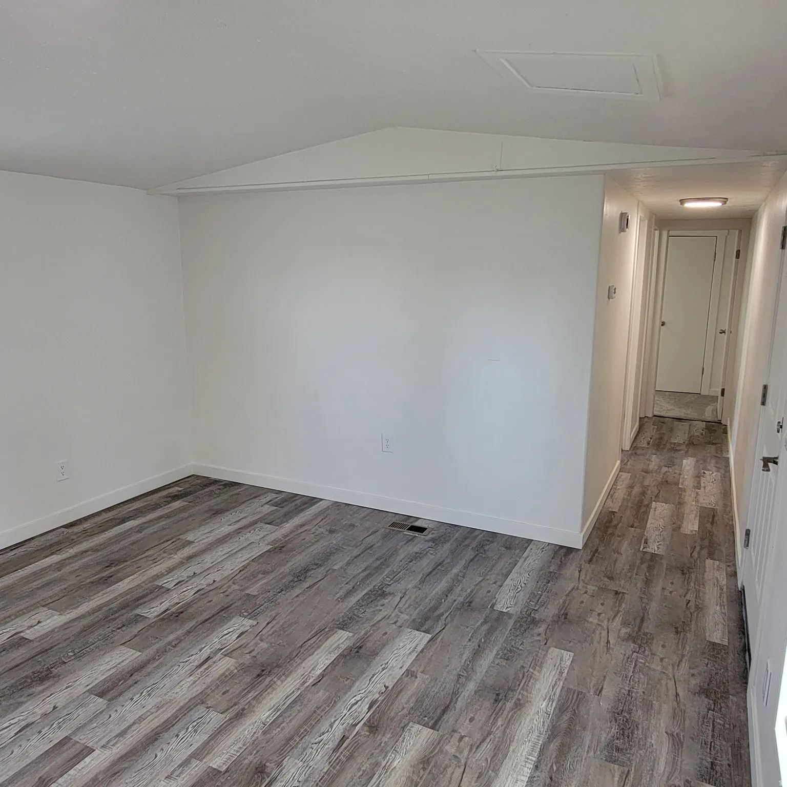 Open interior space featuring wood-finish flooring, white walls, and a hallway with a recessed light fixture