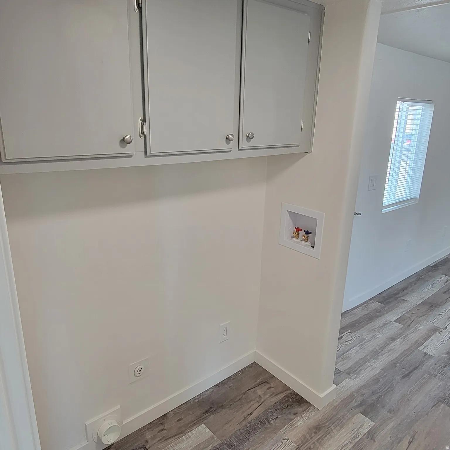 Dedicated laundry area featuring overhead cabinetry with brushed nickel hardware, utility hookups, and wood-finish flooring