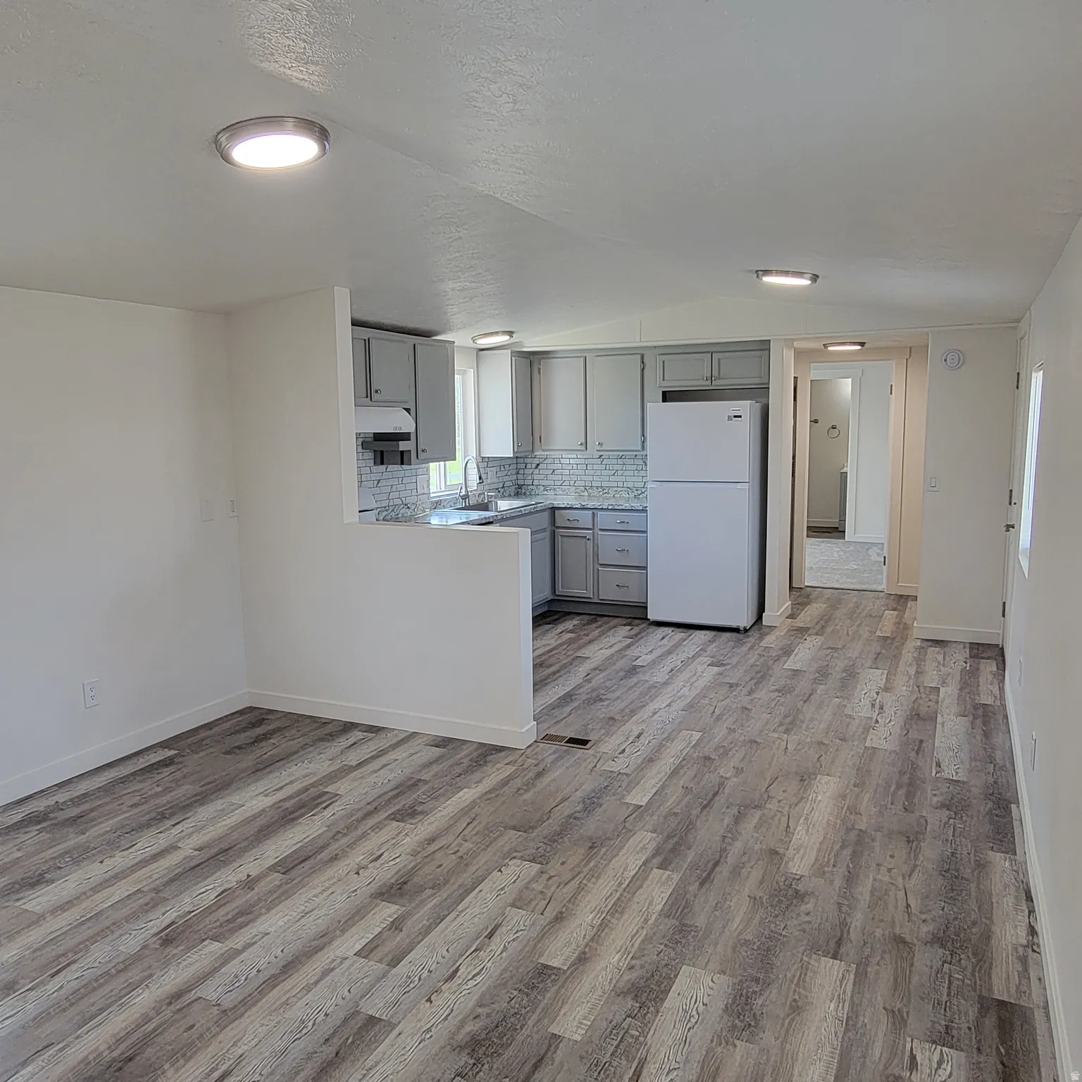 Open-concept living area featuring wood-finish flooring, a kitchen with grey cabinetry, a tile backsplash, and recessed lighting