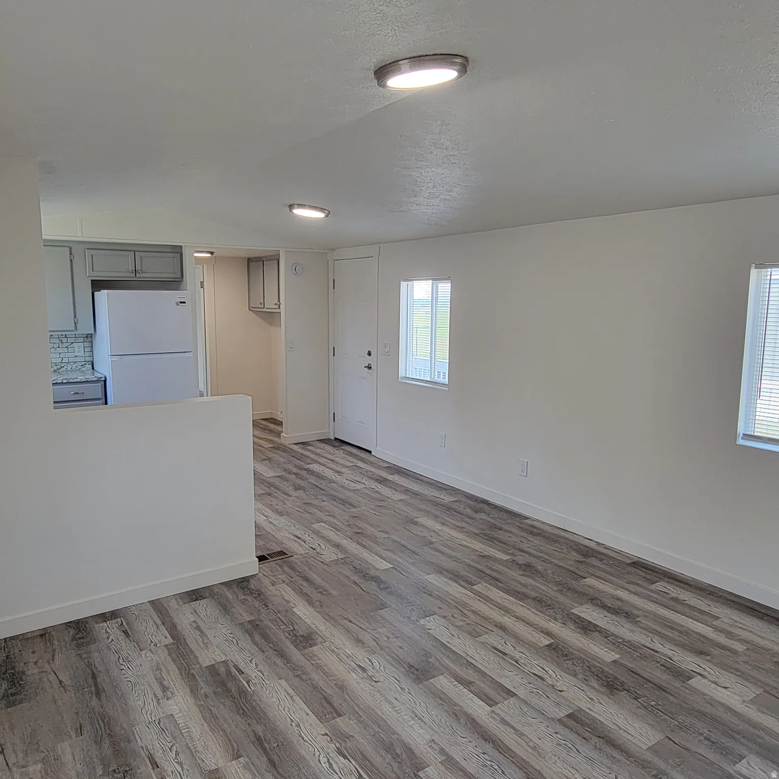 Open-concept living space featuring wood-finish flooring, recessed lighting, white walls, and a partial wall separating the kitchen area