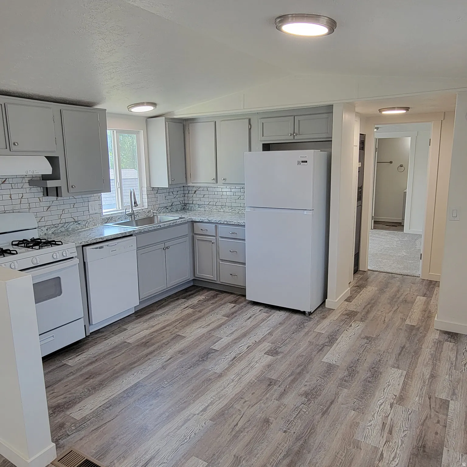 Kitchen featuring white appliances, a stainless steel sink, light grey cabinetry, patterned countertops, and a white subway tile backsplash