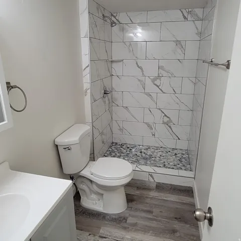 Shower stall featuring rectangular white and gray veined tile walls and a pebble-style floor