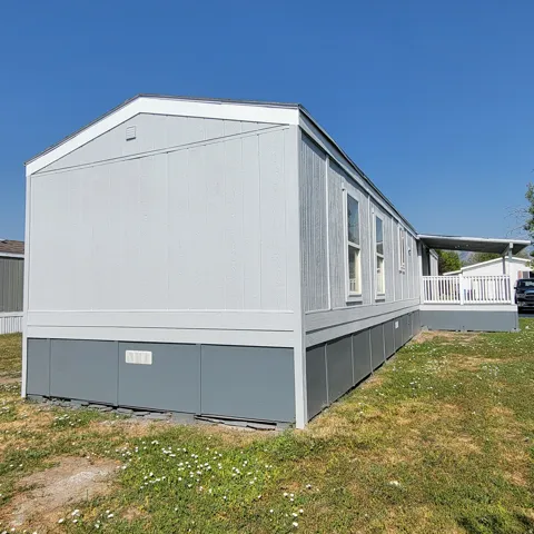 Light gray horizontal siding with white trim, gray skirting, multiple windows, and an attached white-railed porch with a gray floor