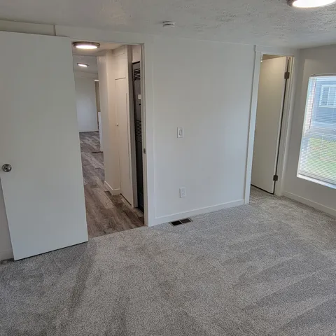 Carpeted room featuring a white interior door with brushed nickel hardware, a window with blinds, and white baseboards