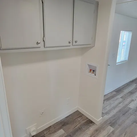 Dedicated laundry area featuring overhead cabinetry with brushed nickel hardware, utility hookups, and wood-finish flooring