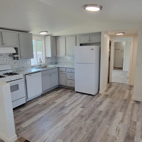 Kitchen featuring white appliances, a stainless steel sink, light grey cabinetry, patterned countertops, and a white subway tile backsplash