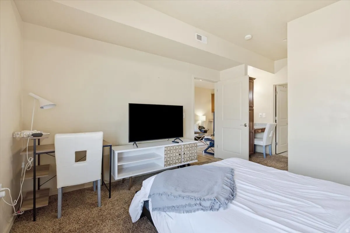 Carpeted interior space featuring a built-in media console, a light-toned desk with shelving, and a flat panel door