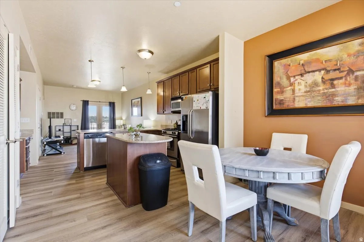 Open-concept living space featuring wood-finish flooring, a kitchen island with stone countertops, stainless steel appliances, and pendant lighting