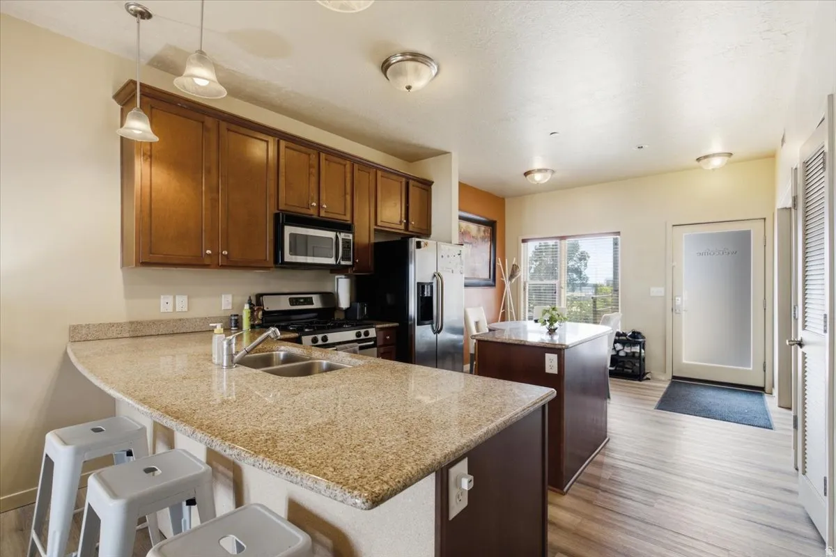 Kitchen featuring granite countertops, wood-finish flooring, stainless steel appliances, and a built-in kitchen island