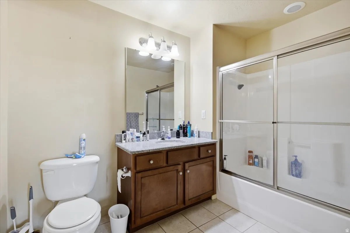 Bathroom featuring a granite-look countertop vanity with wood-finish cabinetry, a glass-enclosed shower-over-tub combination, a recessed ceiling light, and tiled flooring