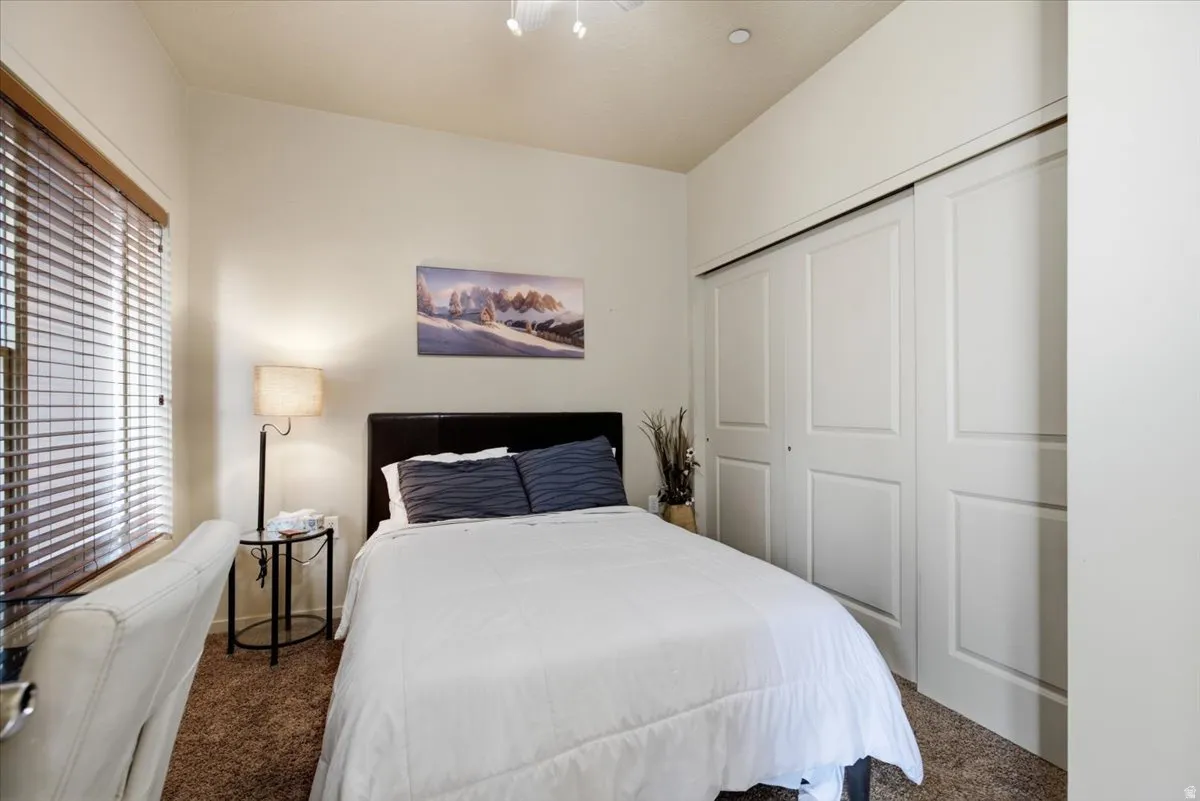 Carpeted bedroom featuring a large window with horizontal blinds, a vaulted ceiling, and sliding bi-fold closet doors