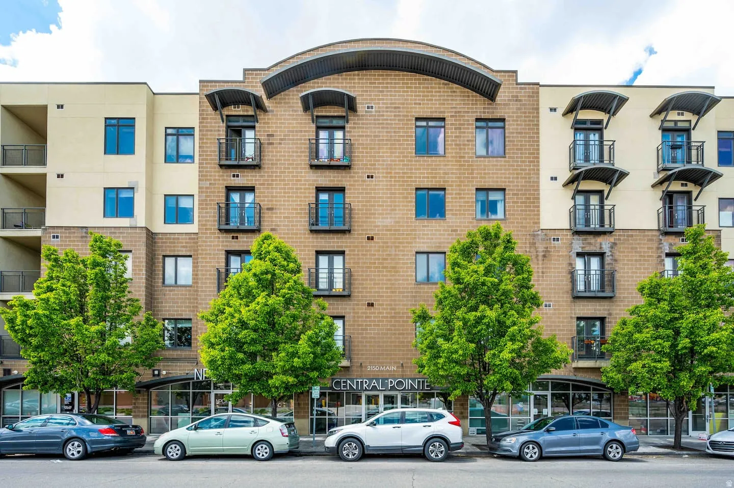 Contemporary multi-story building featuring brick and stucco facade, individual balconies with metal railings, and decorative window awnings