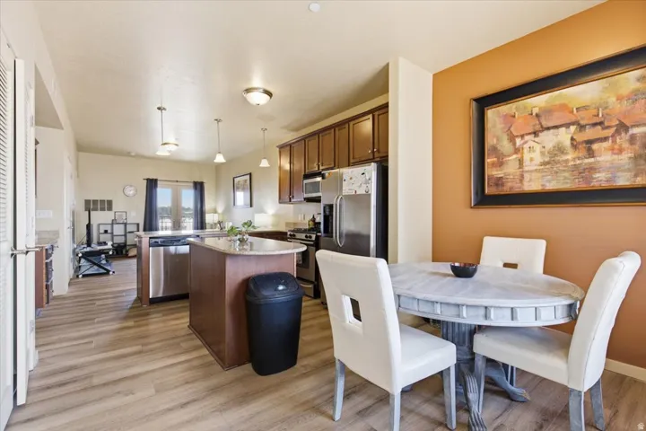 Open-concept living space featuring wood-finish flooring, a kitchen island with stone countertops, stainless steel appliances, and pendant lighting
