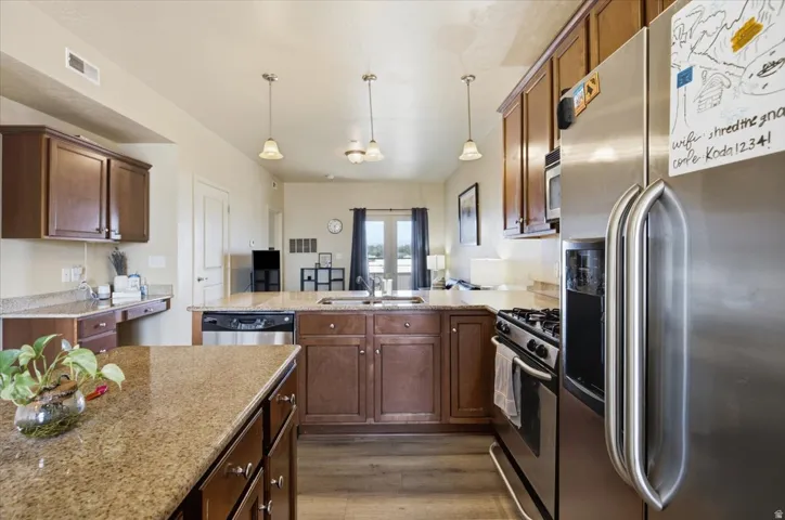 Modern kitchen featuring wood-finish cabinetry, granite countertops, and stainless steel appliances including a refrigerator, dishwasher, and gas range
