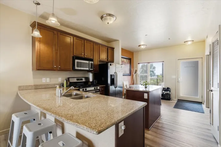 Kitchen featuring granite countertops, wood-finish flooring, stainless steel appliances, and a built-in kitchen island