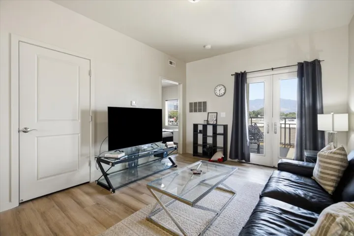 Living area featuring wood-finish flooring, light-toned walls, and a glass-paneled double door leading to an outdoor balcony
