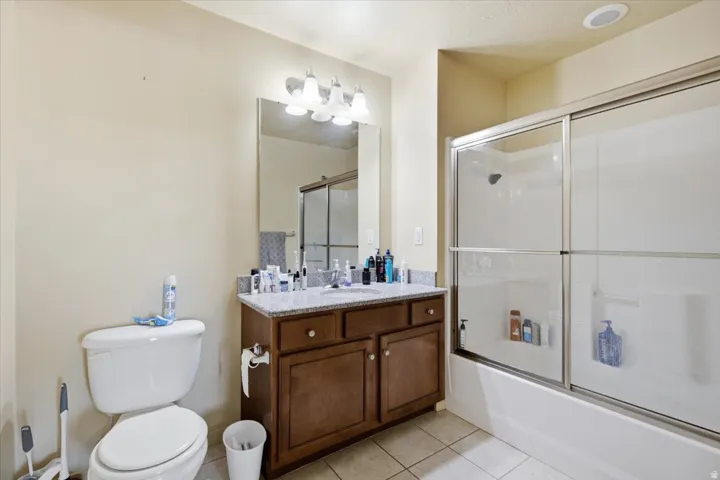 Bathroom featuring a granite-look countertop vanity with wood-finish cabinetry, a glass-enclosed shower-over-tub combination, a recessed ceiling light, and tiled flooring