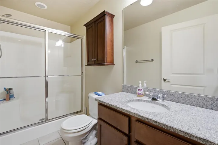 Bathroom featuring a shower with glass enclosure, a toilet, and a vanity with a granite-finish countertop, undermount sink, and wood-finish cabinetry