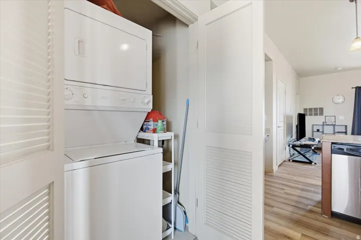Integrated laundry closet featuring a white stackable washer and dryer unit, louvered bi-fold doors, and recessed shelving