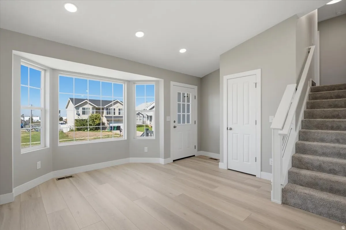 Bay window with multiple panes, light wood-finish flooring, recessed ceiling lighting, and a carpeted staircase with white railing