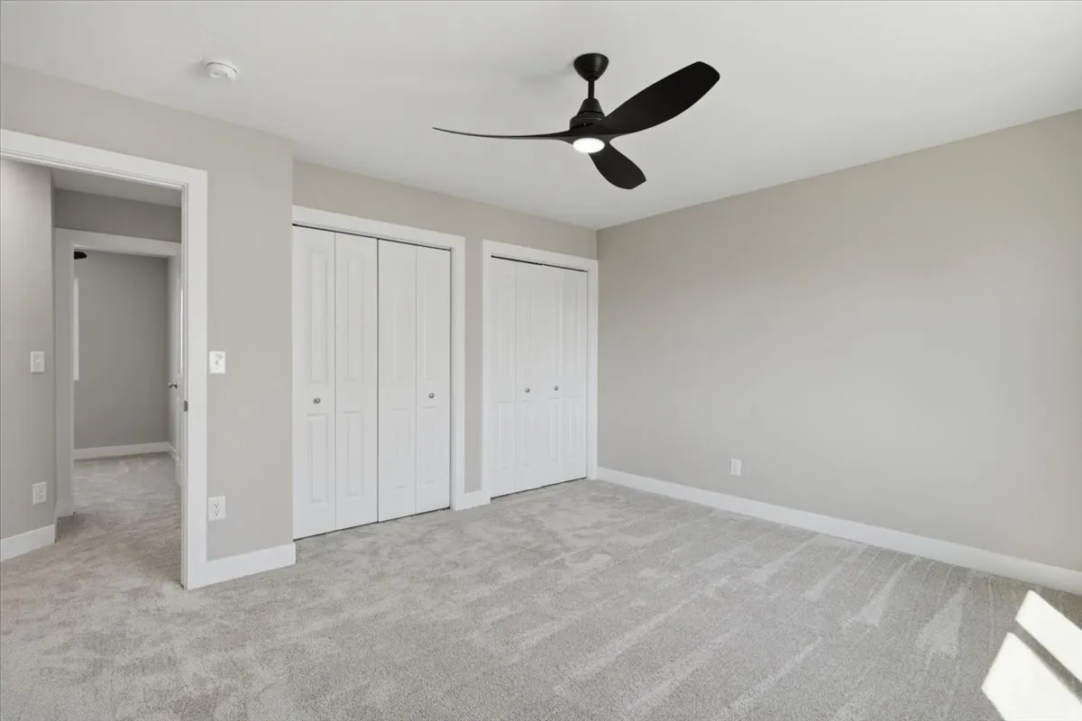 Spacious room featuring light gray carpet flooring, neutral wall tones, white trim, and a contemporary black ceiling fan with integrated lighting