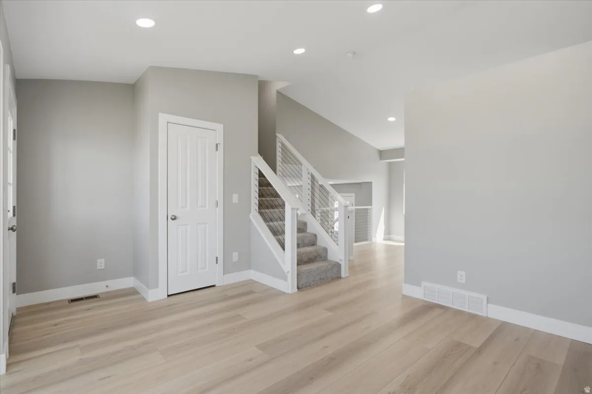 Spacious interior featuring light wood-finish flooring, a contemporary staircase with cable railing, recessed ceiling lighting, a paneled door, and neutral wall tones