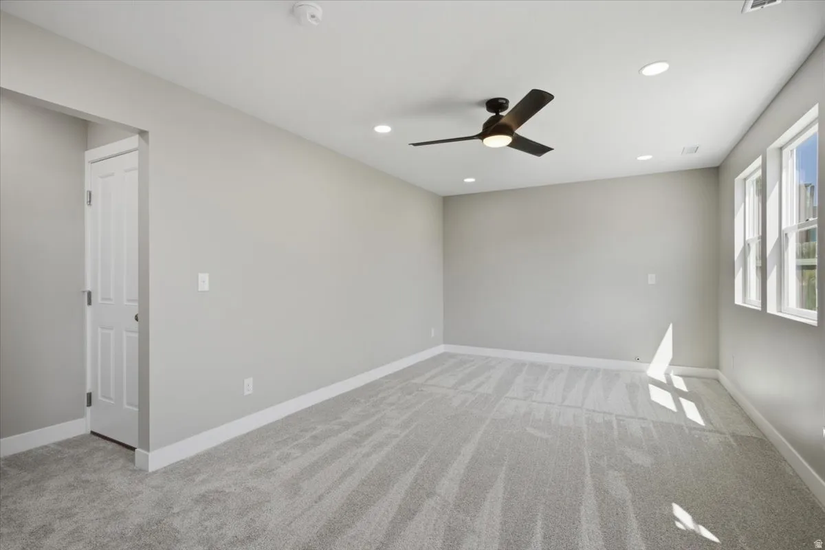 Spacious room featuring light gray carpeting, recessed lighting, a modern ceiling fan, multiple windows, and white trim